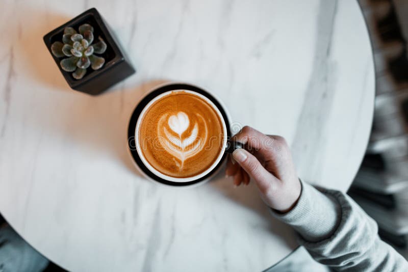 Mani femminili che tengono una tazza di latte sui precedenti della tavola in un caffè Un amante di caffè caldo di mattina gode di fotografia stock libera da diritti