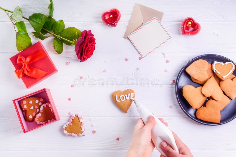 Mani femminili di vista superiore che decorano i biscotti casalinghi nella forma di cuore come regalo per l'amante il giorno del immagine stock libera da diritti