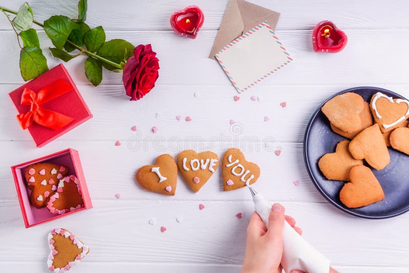 Mani femminili di vista superiore che decorano i biscotti casalinghi nella forma di cuore come regalo per l'amante il giorno del immagine stock libera da diritti