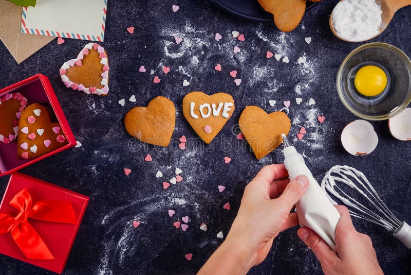 Mani femminili di vista superiore che decorano i biscotti casalinghi nella forma di cuore come regalo per l'amante il giorno del immagine stock libera da diritti