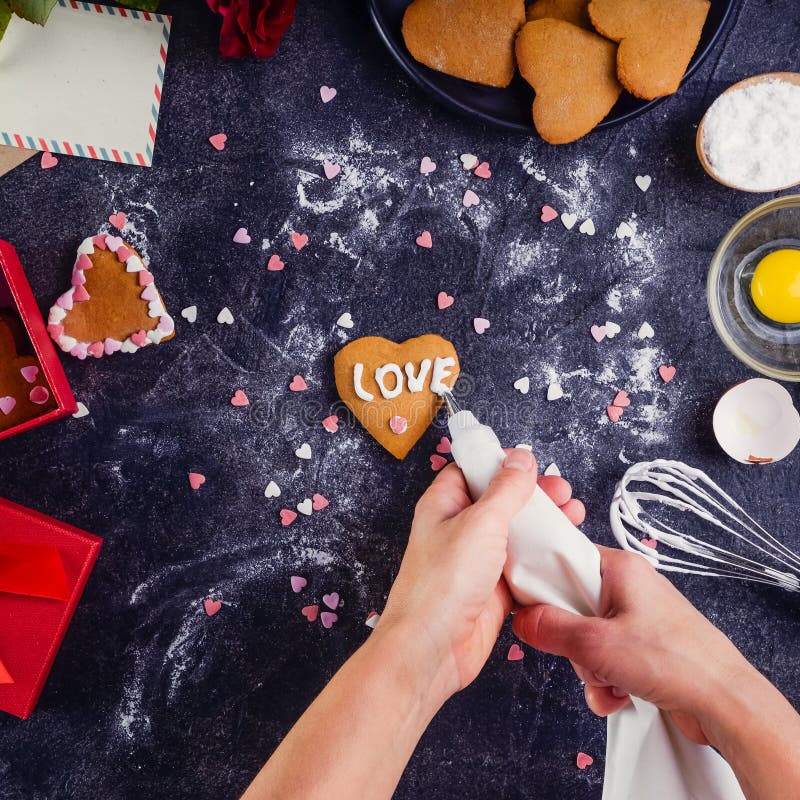 Mani femminili di vista superiore che decorano i biscotti casalinghi nella forma di cuore come regalo per l'amante il giorno del fotografia stock