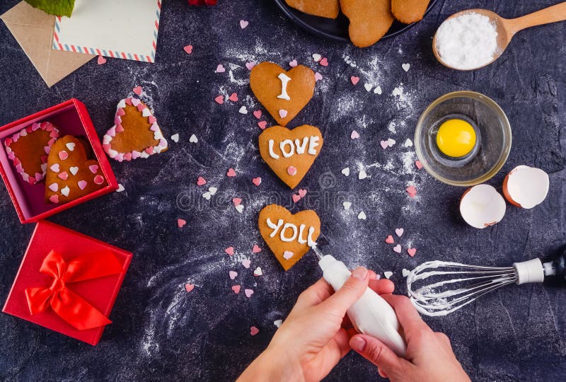 Mani femminili di vista superiore che decorano i biscotti casalinghi nella forma di cuore come regalo per l'amante il giorno del immagini stock libere da diritti