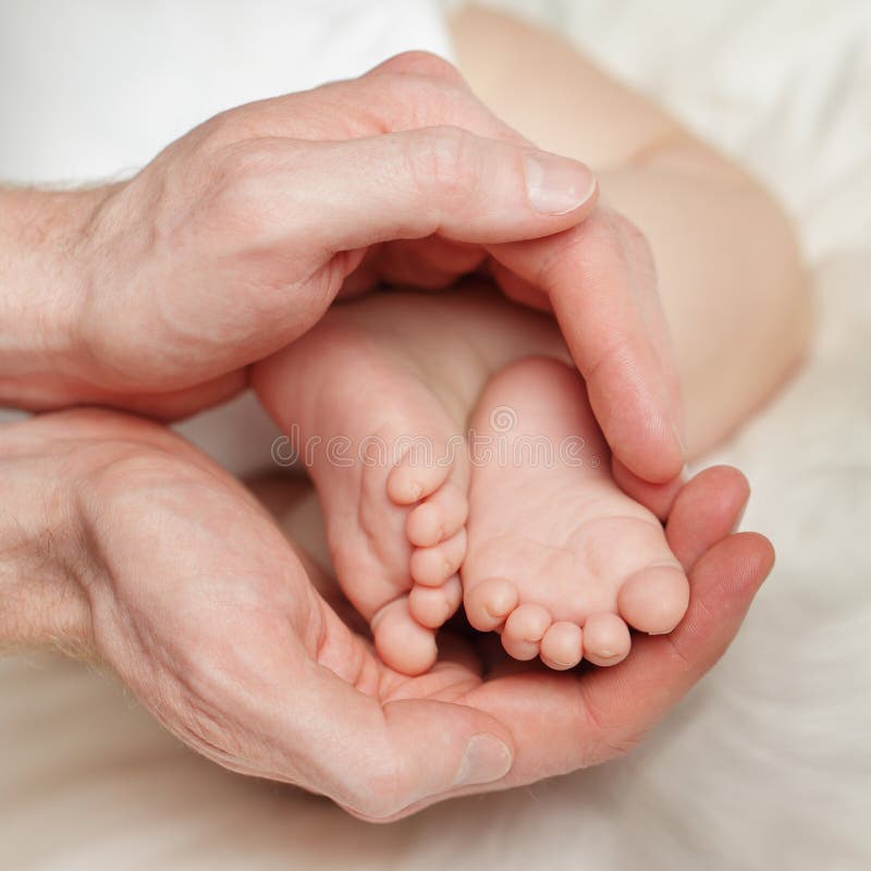 Mani maschii che tengono i piccoli piedi del neonato fotografia stock Mani maschii che tengono i piccoli piedi del neonato fotografia stock