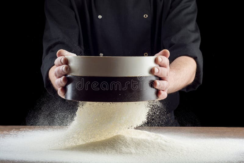 Mani maschii che vagliano farina dal vecchio setaccio sul vecchio tavolo da cucina di legno Su fondo nero fotografie stock libere da diritti Mani maschii che vagliano farina dal vecchio setaccio sul vecchio tavolo da cucina di legno Su fondo nero fotografie stock libere da diritti