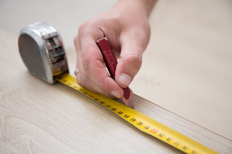 Mani maschii con nastro adesivo di misurazione ed il nuovo pavimento di legno laminato immagine stock Mani maschii con nastro adesivo di misurazione ed il nuovo pavimento di legno laminato immagine stock