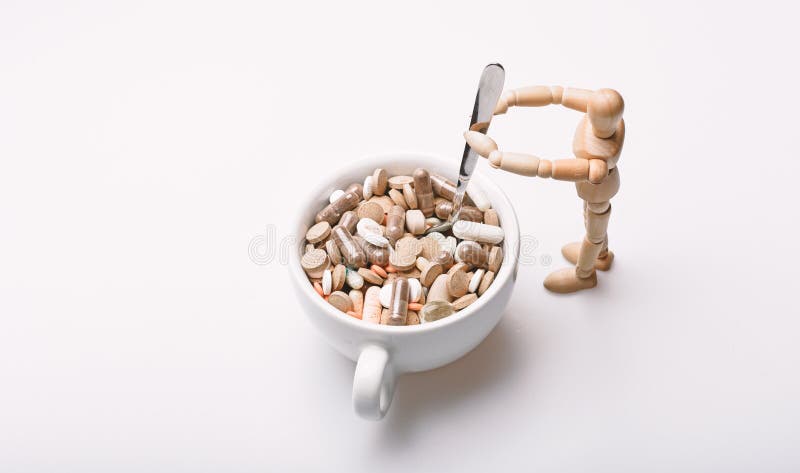Manichino umano di legno vicino alle pillole ed alle compresse piene della tazza Prenda il concetto della medicina Cocktail della immagine stock