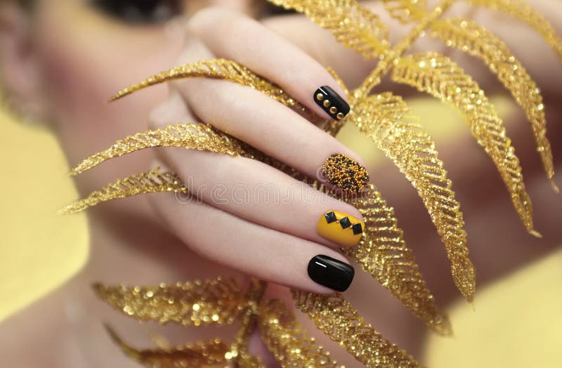 Caviar manicure in yellow black nails with black and gold rhinestones with brilliant ornament in his hand. Caviar manicure in yellow black nails with black and gold rhinestones with brilliant ornament in his hand.