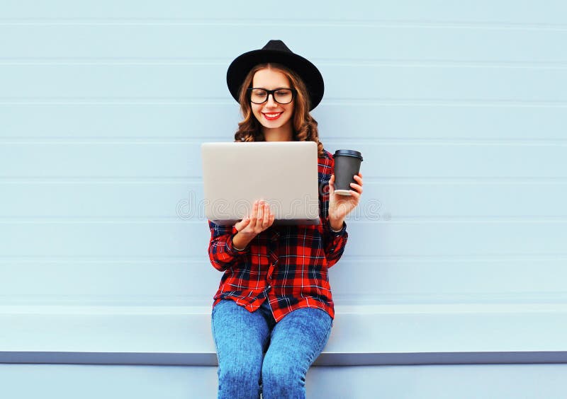 Manier jonge glimlachende vrouw die laptop computer met koffiekop met behulp van die in openlucht in stad rusten, die zwart hoede royalty-vrije stock afbeeldingen Manier jonge glimlachende vrouw die laptop computer met koffiekop met behulp van die in openlucht in stad rusten, die zwart hoede royalty-vrije stock afbeeldingen