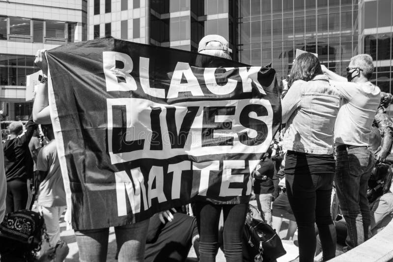 Two women drape a Black Live Matter flag around themselves in protest of the death of George Floyd and police brutality, in front of the Ohio Statehouse.  Downtown Columbus, OH. May 30th 2020. Two women drape a Black Live Matter flag around themselves in protest of the death of George Floyd and police brutality, in front of the Ohio Statehouse.  Downtown Columbus, OH. May 30th 2020.