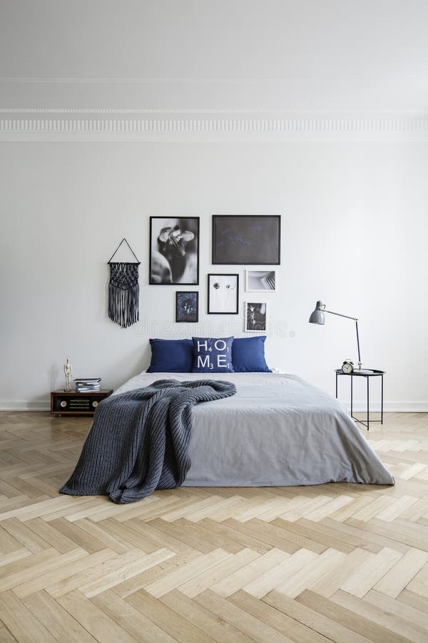 Manifesti sopra il letto grigio sul pavimento di legno nell'interno bianco spazioso della camera da letto con la lampada Foto rea immagine stock libera da diritti