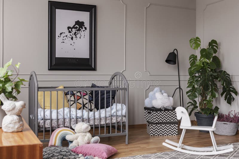 Manifesto sopra la culla accanto ai giocattoli nell'interno della camera da letto del bambino grigio con la pianta ed il cavallo