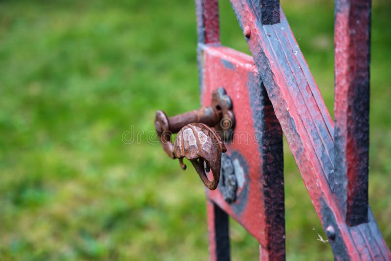 Manija del hierro labrado en una vieja puerta de jardín abierta con la cuesta roja gastada imagen de archivo Manija del hierro labrado en una vieja puerta de jardín abierta con la cuesta roja gastada imagen de archivo