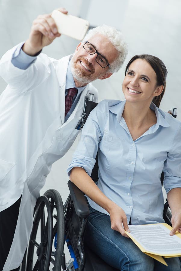 Smilng doctor taking selfies with a patient in wheelchair using a smart phone, care and disability integration concept. Smilng doctor taking selfies with a patient in wheelchair using a smart phone, care and disability integration concept
