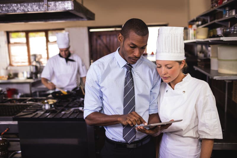 Manlig chef och kvinnlig kock som använder den digitala minnestavlan i kök arkivfoto Manlig chef och kvinnlig kock som använder den digitala minnestavlan i kök arkivfoto