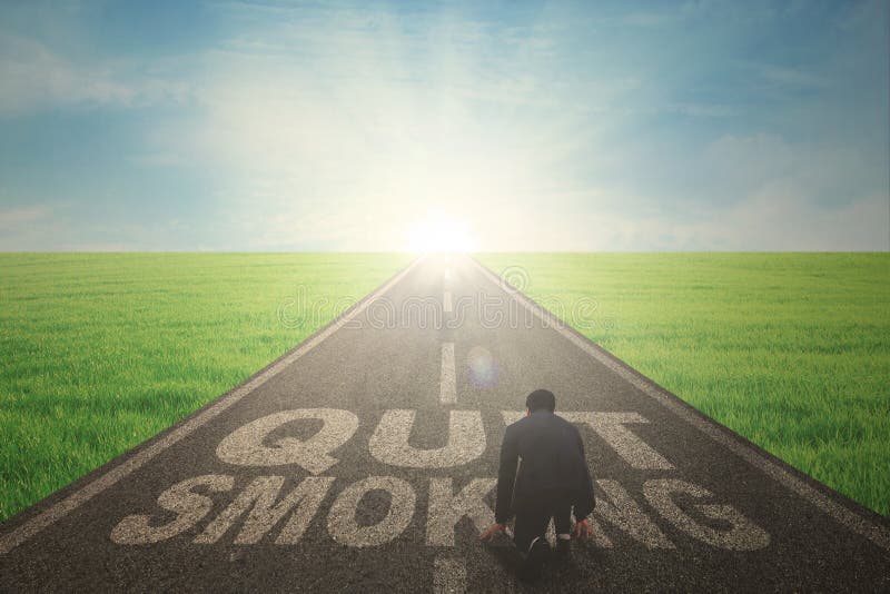 Back view of a male manager wearing a formal suit while kneeling over the text of quit smoking on the road. Back view of a male manager wearing a formal suit while kneeling over the text of quit smoking on the road