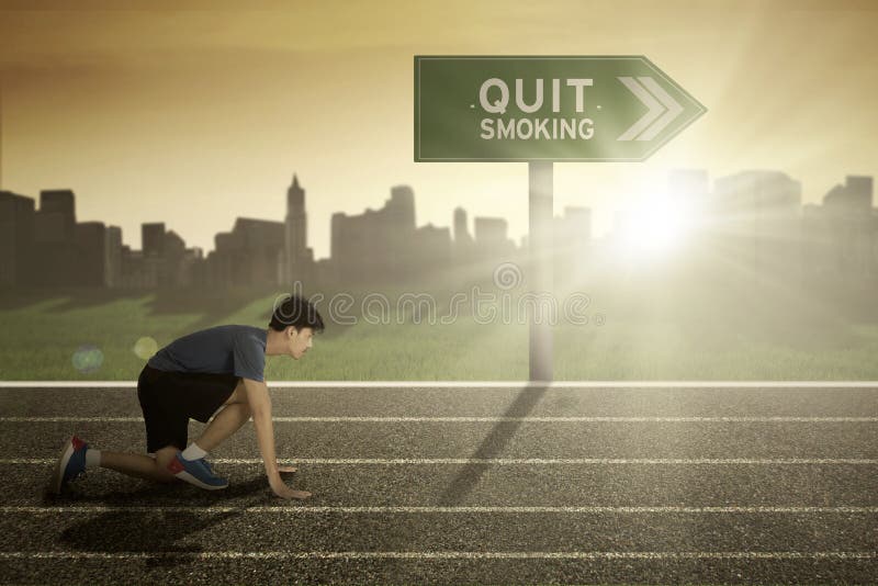 Male runner with quit smoking word on signpost while ready to run in the track. Male runner with quit smoking word on signpost while ready to run in the track