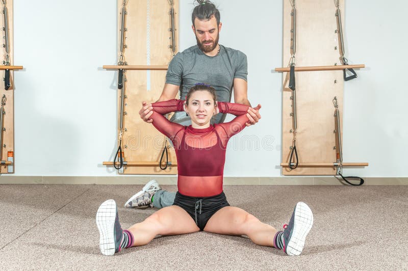 Manlig personlig instruktör för stilig yoga med ett skägg som hjälper den unga konditionflickan att sträcka hennes muskler efter royaltyfria foton Manlig personlig instruktör för stilig yoga med ett skägg som hjälper den unga konditionflickan att sträcka hennes muskler efter royaltyfria foton