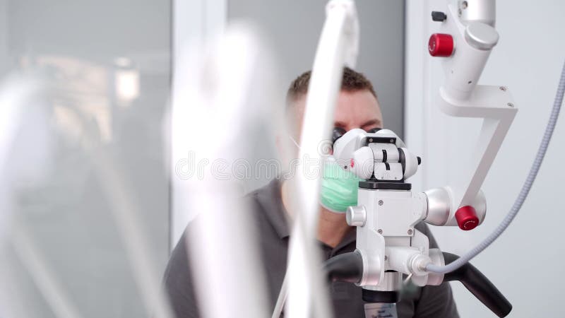 Manlig tandläkare som behandlar patienter som använder mikroskop på det moderna tandläkarkontoret. Läkaren arbetar med mikroskopin