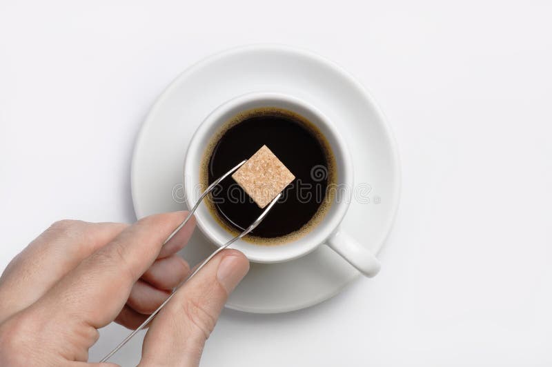 Manlig tång för handinnehavsocker med kuben för rottingsocker över koppen av svart kaffe mot bästa sikt för vit bakgrund med utry royaltyfri bild Manlig tång för handinnehavsocker med kuben för rottingsocker över koppen av svart kaffe mot bästa sikt för vit bakgrund med utry royaltyfri bild