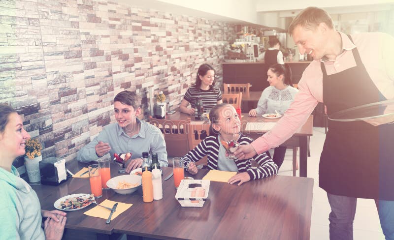 Manlig uppassare som tjänar som den gladlynta familjen i familjkafé royaltyfri fotografi Manlig uppassare som tjänar som den gladlynta familjen i familjkafé royaltyfri fotografi