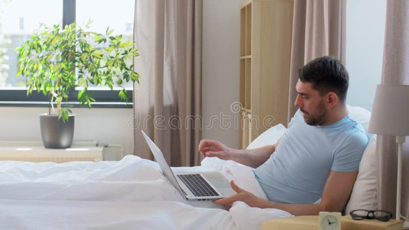 Mann in Brille mit Laptop aus dem Bett