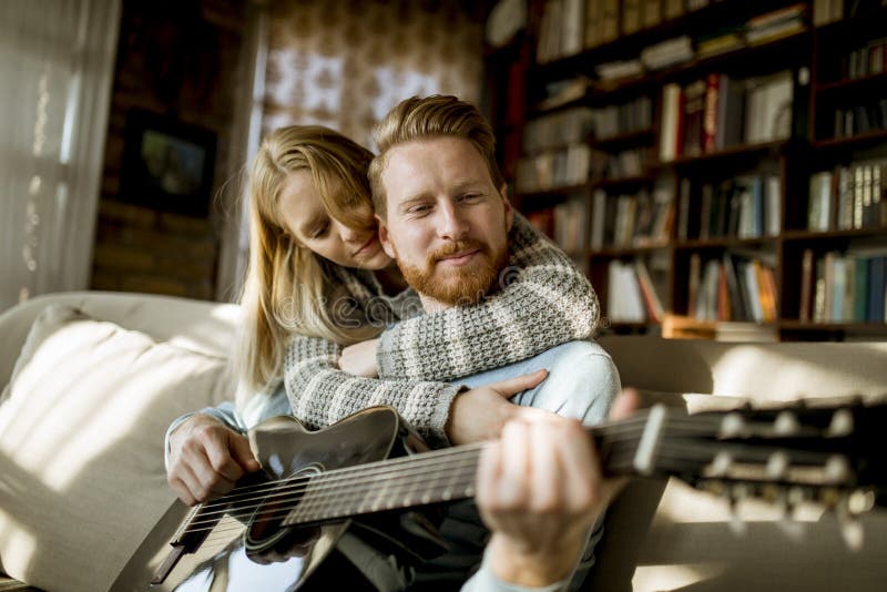 Mann, der Akustikgitarre auf Sofa für seine junge Schönheit spielt lizenzfreies stockfoto Mann, der Akustikgitarre auf Sofa für seine junge Schönheit spielt lizenzfreies stockfoto