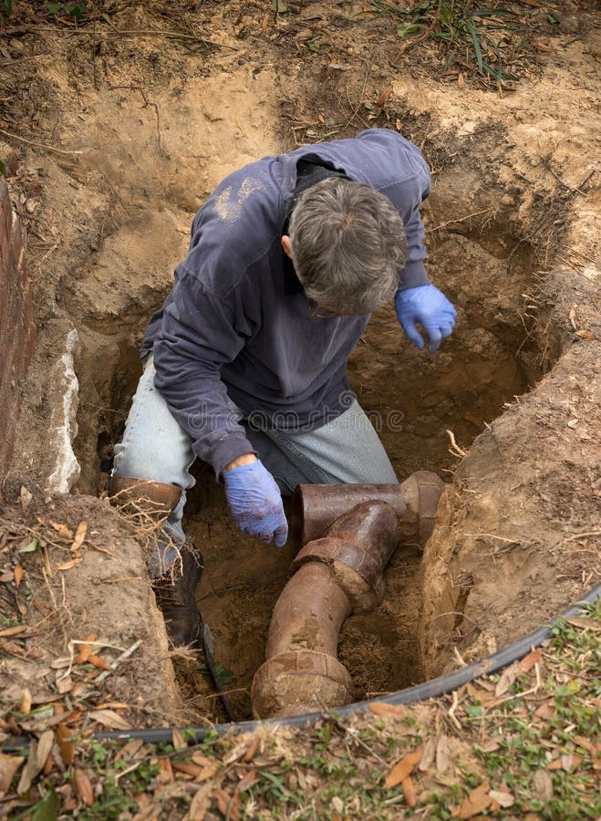 Man in a hole in the earth examining old clay sewer pipes that are infested with tree roots. Man in a hole in the earth examining old clay sewer pipes that are infested with tree roots.