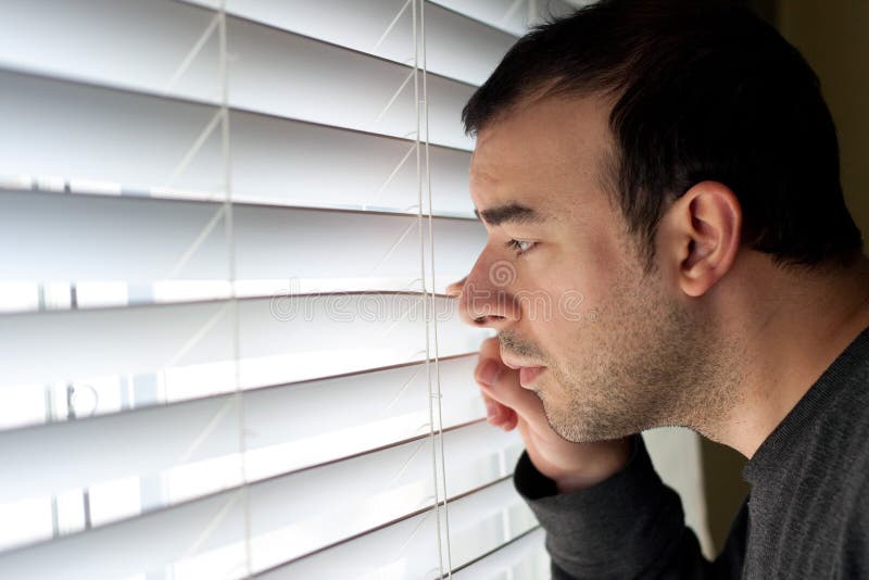 Scared or annoyed man peeks out the window through the blinds. Scared or annoyed man peeks out the window through the blinds.