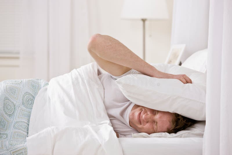 Mann, der Kissen verwendet, um Geräusche heraus zu blocken lizenzfreies stockbild Mann, der Kissen verwendet, um Geräusche heraus zu blocken lizenzfreies stockbild