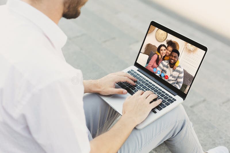 Mann, der mit einer Multirasse-Familie Videoanrufe führt, während er mit einem Laptop im Freien sitzt stockfoto