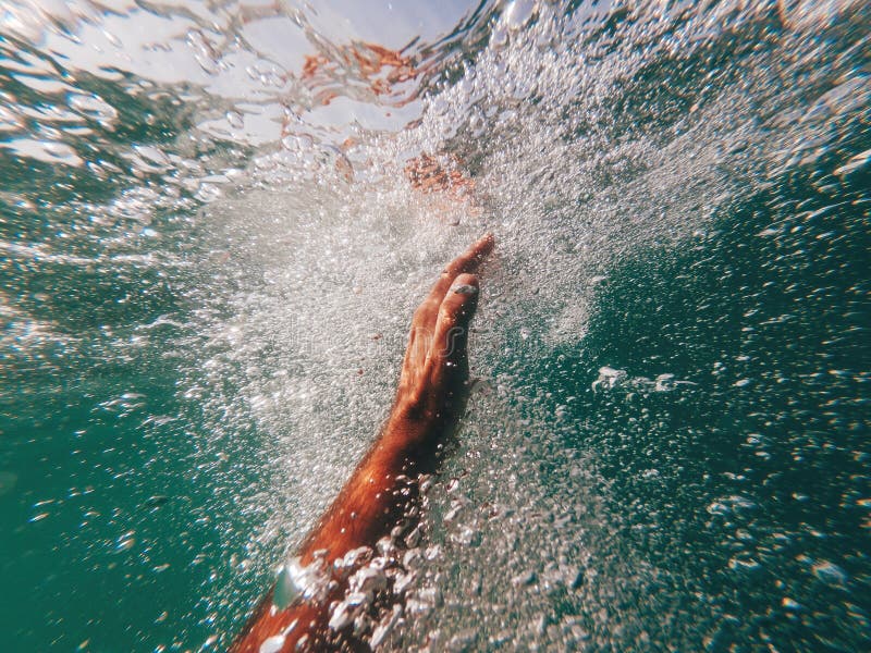 Man drowning in deep blue sea, close up of hand reaching to the ocean surface, surrounded with air bubble, swimmer fighting for his life, selective focus. Man drowning in deep blue sea, close up of hand reaching to the ocean surface, surrounded with air bubble, swimmer fighting for his life, selective focus