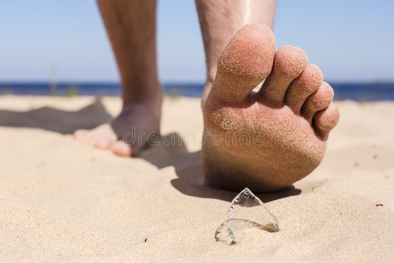 Man goes on the beach and the risk of stepping on a splinter of broken bottle glass, which is lying on the sand littered in places with poor environmental conditions. Man goes on the beach and the risk of stepping on a splinter of broken bottle glass, which is lying on the sand littered in places with poor environmental conditions