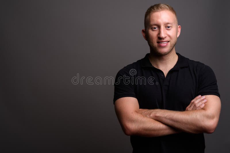Mann mit dem blonden Haar, das schwarzes Polohemd gegen graues backgr trägt stockfotos Mann mit dem blonden Haar, das schwarzes Polohemd gegen graues backgr trägt stockfotos