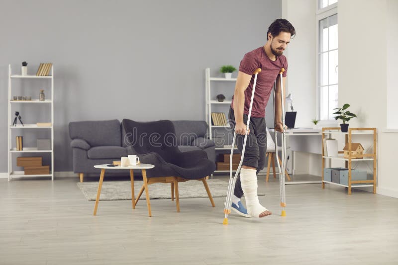 Successful rehabilitation and recovery of people after physical injury such as bone fracture in car or home accident: Young man with broken leg trying to walk with crutches and making good progress. Successful rehabilitation and recovery of people after physical injury such as bone fracture in car or home accident: Young man with broken leg trying to walk with crutches and making good progress