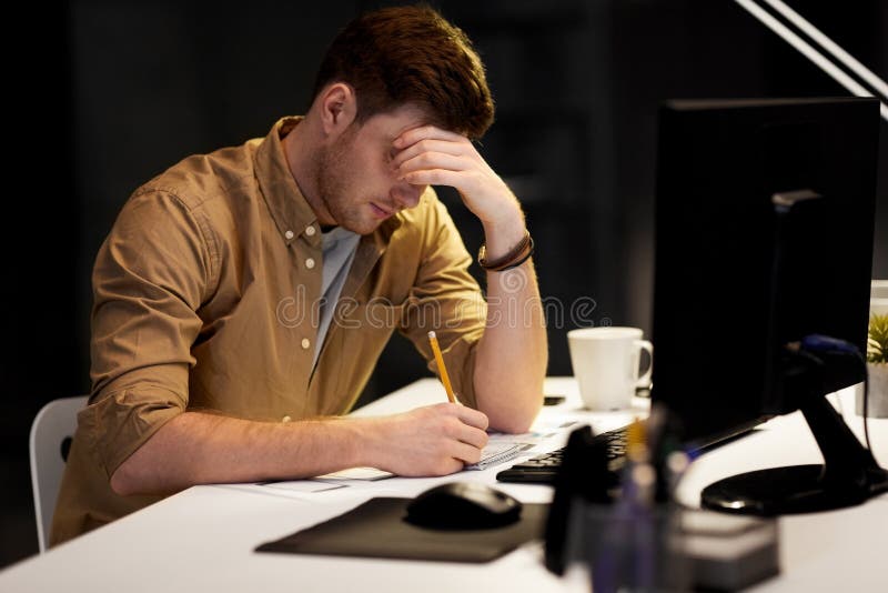 Business, deadline and people concept - man with notepad and computer working late at night office. Business, deadline and people concept - man with notepad and computer working late at night office