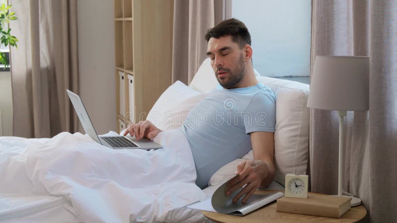 Mann mit Laptop, der im Schlafzimmer arbeitet