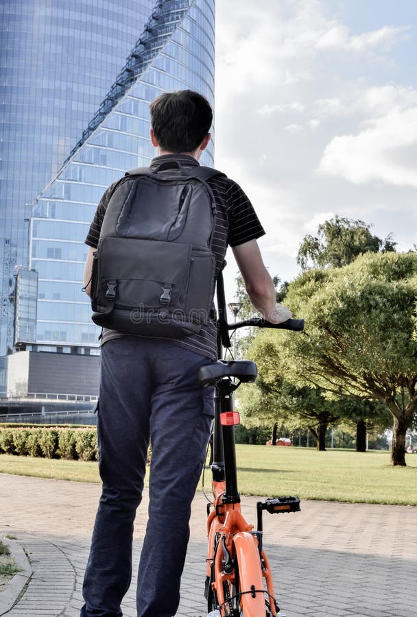 Mann mit Rucksack steht mit einem Fahrrad vor der Kulisse eines Bürogebäudes. Student kam zum Lernen. Mitfahrer stockbild