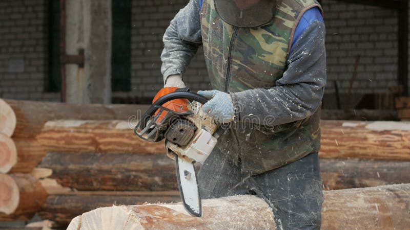 Mann schneidet hölzerne Kettensäge für zukünftiges Haus Schützende Gesichtsmaske auf dem Gesicht des Erbauers und vielen Sägemehl