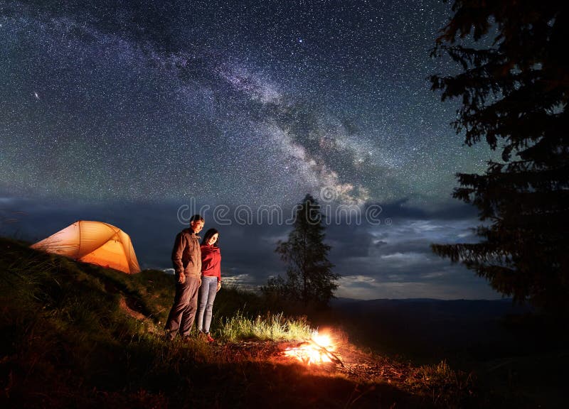 Mann und Frau stehen Campingplatz bereit und betrachten Feuer unter dem sternenklaren Himmel lizenzfreies stockfoto Mann und Frau stehen Campingplatz bereit und betrachten Feuer unter dem sternenklaren Himmel lizenzfreies stockfoto