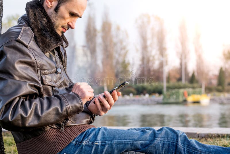 Mann in ungezwungener Kleidung mit Mobiltelefon in einem Park lizenzfreie stockfotografie