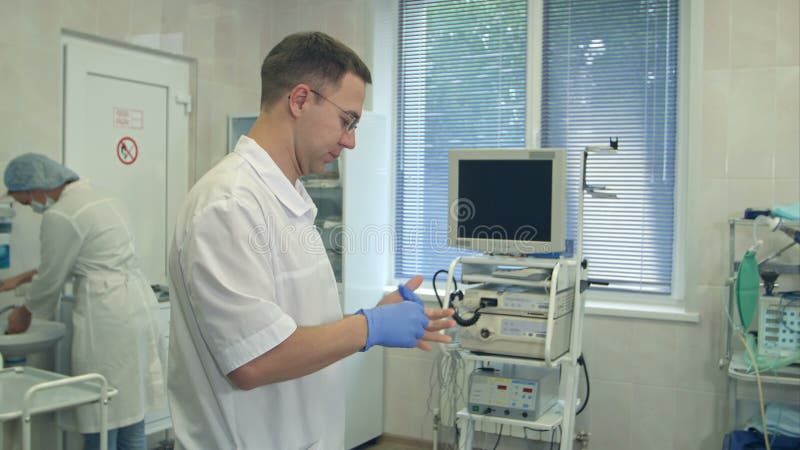Mannelijke chirurg die steriele rubberhandschoenen voor chirurgie aantrekt terwijl de verpleegkundige haar handen in een operatie