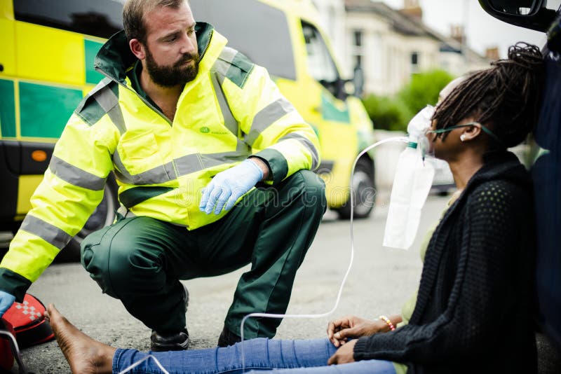 Mannelijke paramedicus die op een zuurstofmasker aan een verwonde vrouw op een weg zetten royalty-vrije stock afbeelding Mannelijke paramedicus die op een zuurstofmasker aan een verwonde vrouw op een weg zetten royalty-vrije stock afbeelding