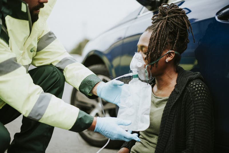 Mannelijke paramedicus die op een zuurstofmasker aan een verwonde vrouw op een weg zetten stock afbeelding Mannelijke paramedicus die op een zuurstofmasker aan een verwonde vrouw op een weg zetten stock afbeelding