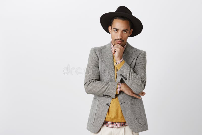 Mannen får allvarlig, när det kommer till jobbet Stående av den snygga fokuserade unga mörkhyade mannen i stilfull hatt och royaltyfri fotografi Mannen får allvarlig, när det kommer till jobbet Stående av den snygga fokuserade unga mörkhyade mannen i stilfull hatt och royaltyfri fotografi