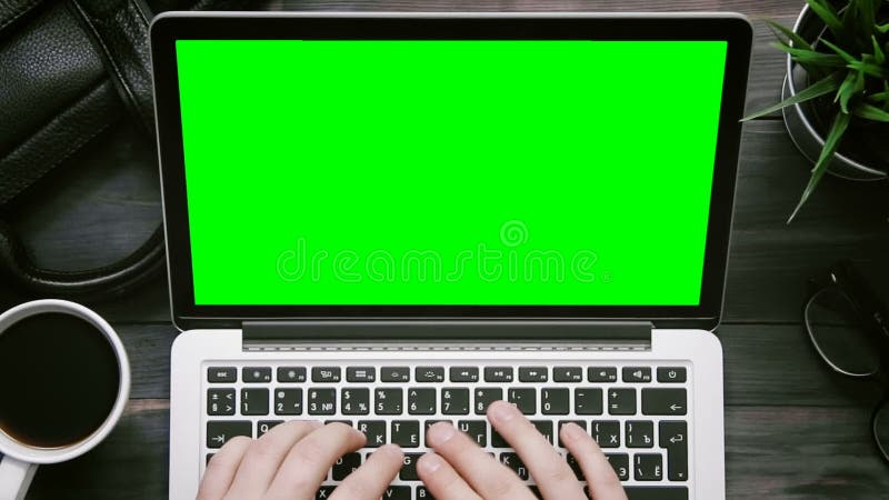 Mannen för den bästa sikten räcker arbete på bärbar datordatoren med den gröna skärmen på det vita skrivbordet från över