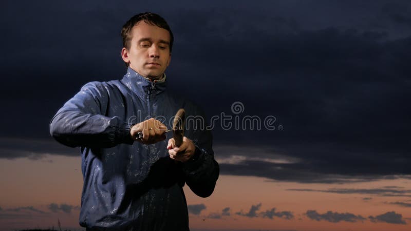 Mannen förbereder trä-ull med jaktkniven för att starta brand på solnedgången på fältet raka trä överlevnadbegrepp