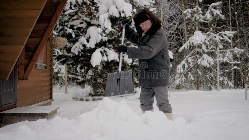 Mannen gör ren gården med en skyffel från högarna av insnöat vintern