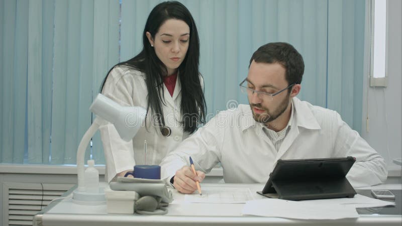Mannen och kvinnliga doktorer diskuterar det medicinska dokumentet royaltyfri fotografi Mannen och kvinnliga doktorer diskuterar det medicinska dokumentet royaltyfri fotografi