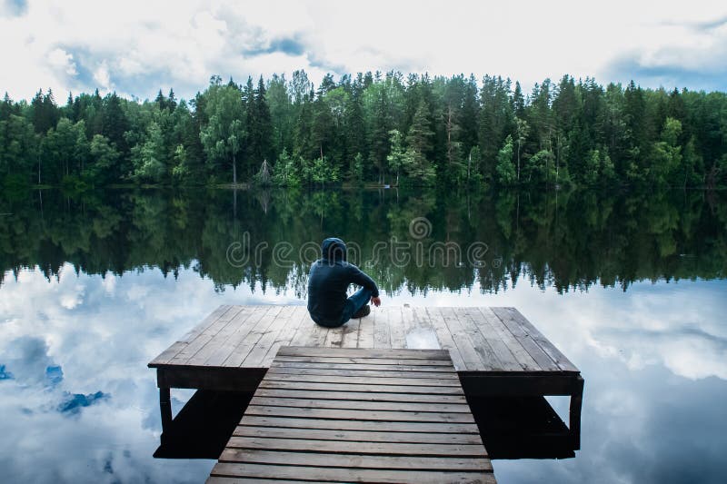 Mannen sitter på pir av en härlig sjö Begreppet av frihet och självständighet, royaltyfri fotografi Mannen sitter på pir av en härlig sjö Begreppet av frihet och självständighet, royaltyfri fotografi