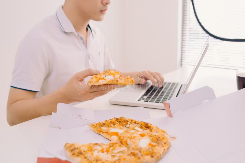 Mannetje die freelancer pizza eten terwijl thuis het werken van bureau stock fotografie Mannetje die freelancer pizza eten terwijl thuis het werken van bureau stock fotografie